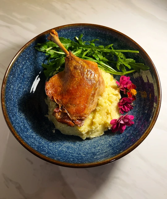 Duck leg confit served on mashed potatoes with herbs
